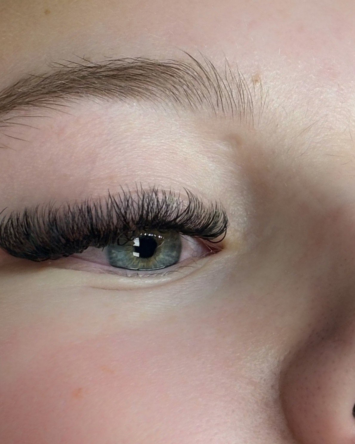 Close-up van een oog met volle, donkere wimperextensions en een verzorgde wenkbrauw