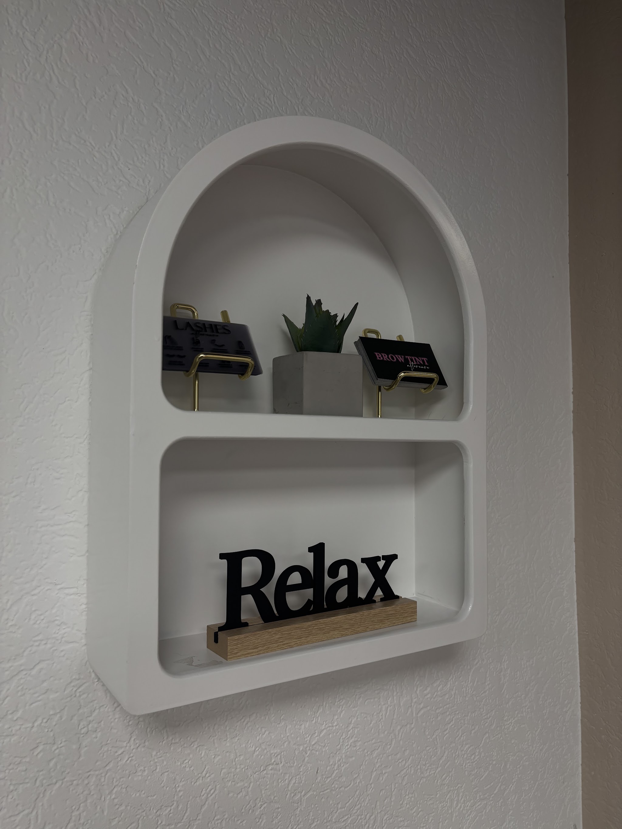 Witte wandnis met boogvorm in de salon, met een plantje en het woord Relax